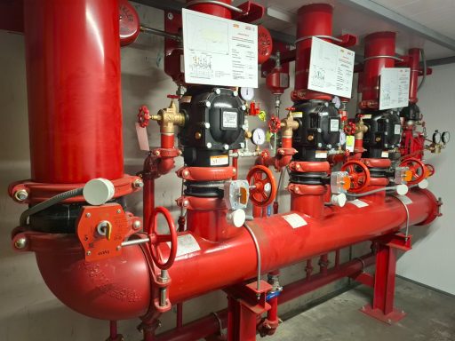 Sistema de bombas de incendios en tuberías rojas, con manómetros y válvulas.